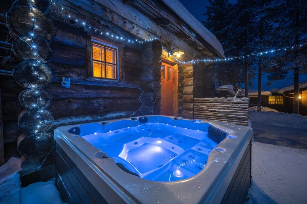 A lit hot tub on the terrace of a log cabin at a snowy accommodation in Saariselkä.