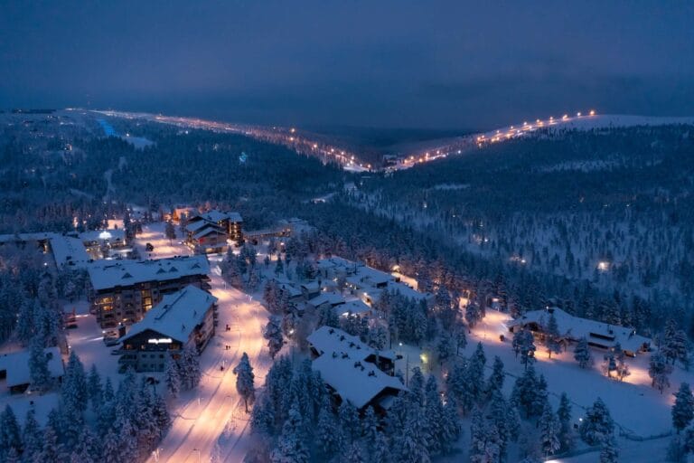Saariselän tunturimaisema iltahämärässä, lumiset rakennukset ja valaistu tie näkyvät ylhäältä päin.